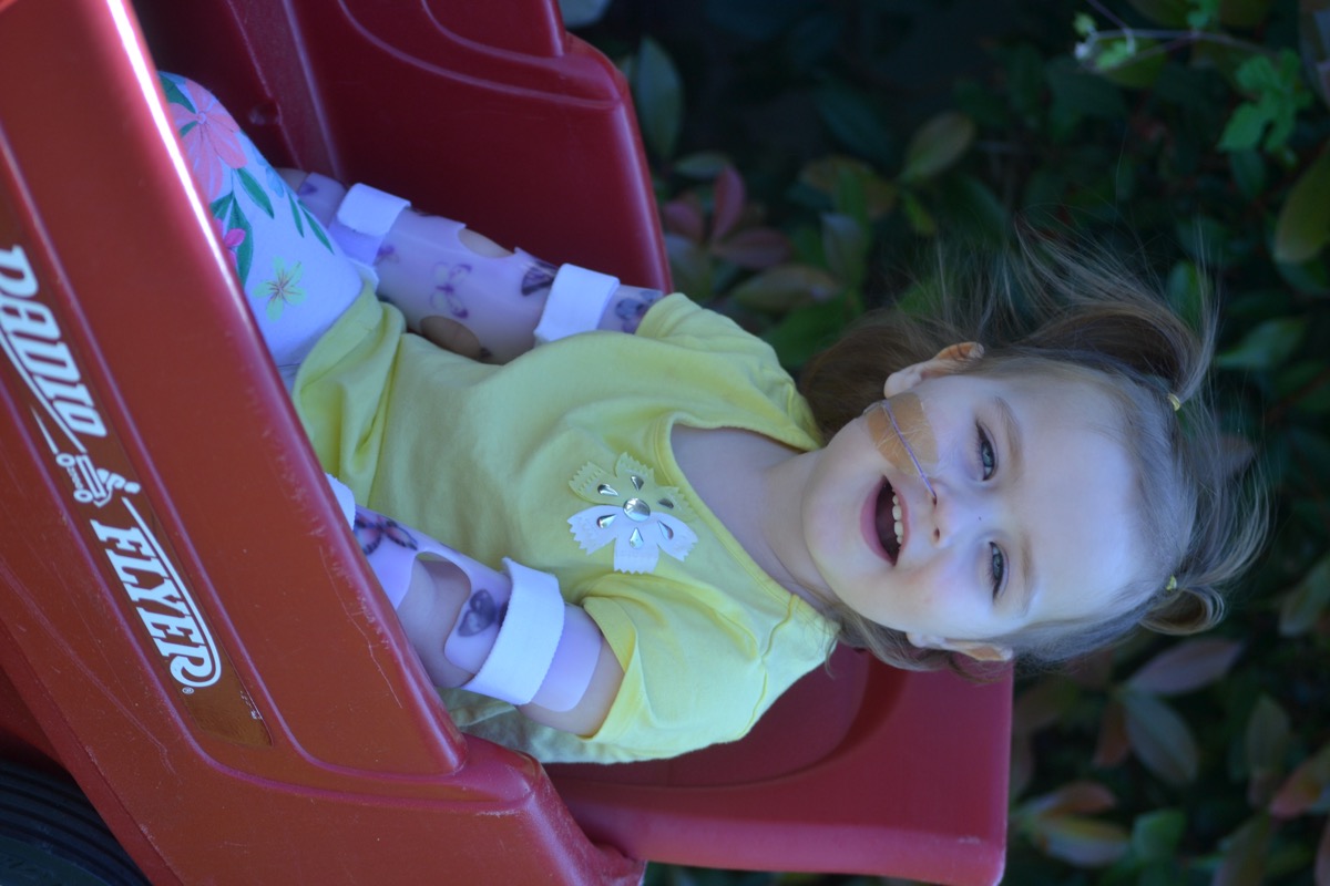 Sophia sitting in a red wagon with an NG tube in 2017