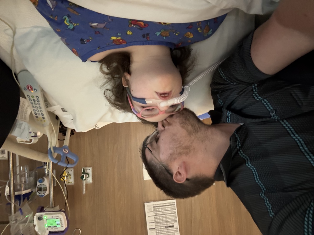 Dad kissing Sophia while staying beside her during a hospital stay in 2025